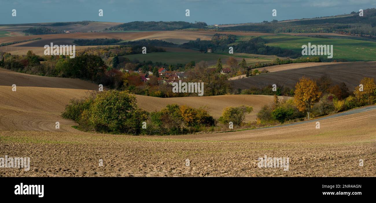 Ein mährisches Dorf zwischen Ackerfeldern mit einer Ziegelwindmühle im Hintergrund. Tschechische republik, Mährisch, Tschechische republik Stockfoto
