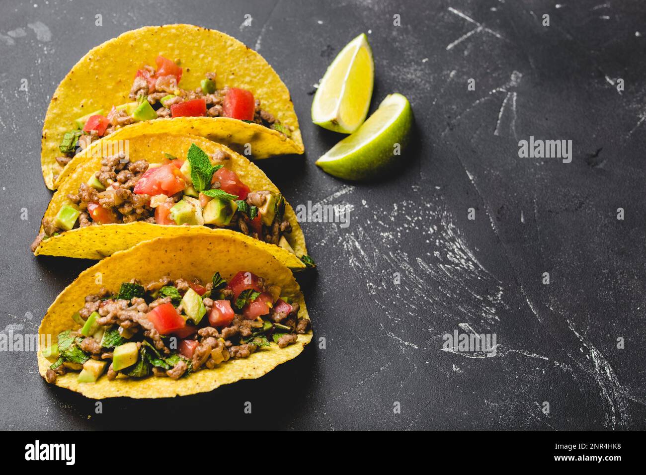 Blick von oben auf mexikanische Tacos mit Fleisch, Tomatensalsa, Avocado, Kräutern in gelber Maistortilla auf schwarzem rustikalem Steinhintergrund mit Kopierbereich. Stockfoto