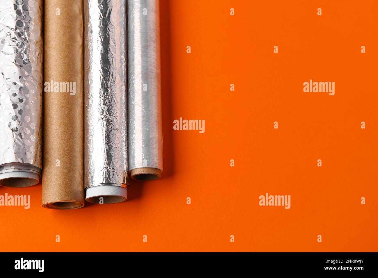 Rollen aus Aluminiumfolie, Backpapier und Lebensmittelfolie auf farbigem Hintergrund Stockfoto
