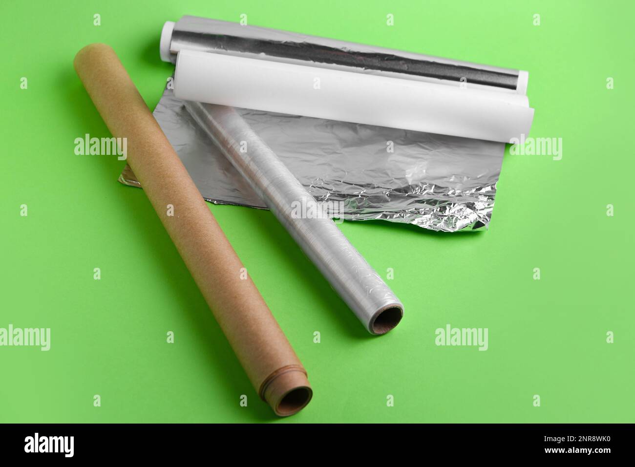 Rollen aus Aluminiumfolie, Backpapier und Lebensmittelfolie auf grünem Hintergrund Stockfoto