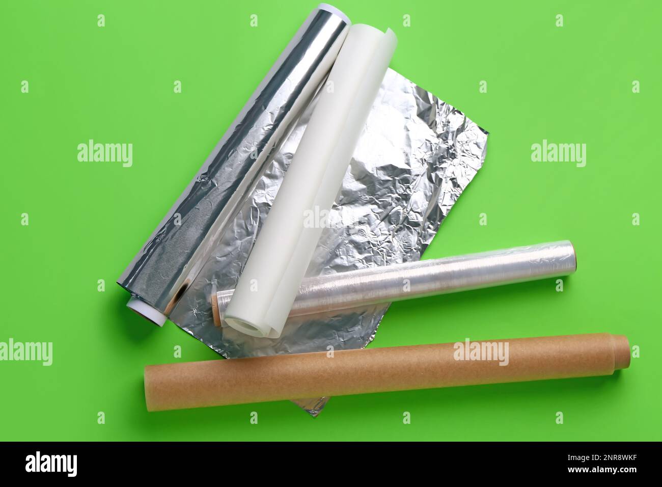 Rollen aus Aluminiumfolie, Backpapier und Lebensmittelfolie auf grünem Hintergrund Stockfoto