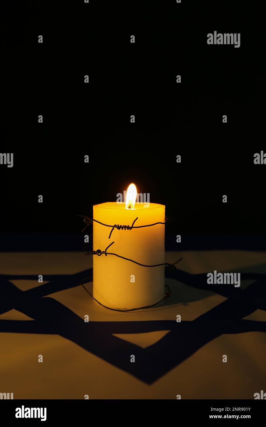 Brennende Kerze mit Stacheldraht auf der Flagge Israels vor dunklem Hintergrund. Internationaler Holocaust-Gedenktag Stockfotografie