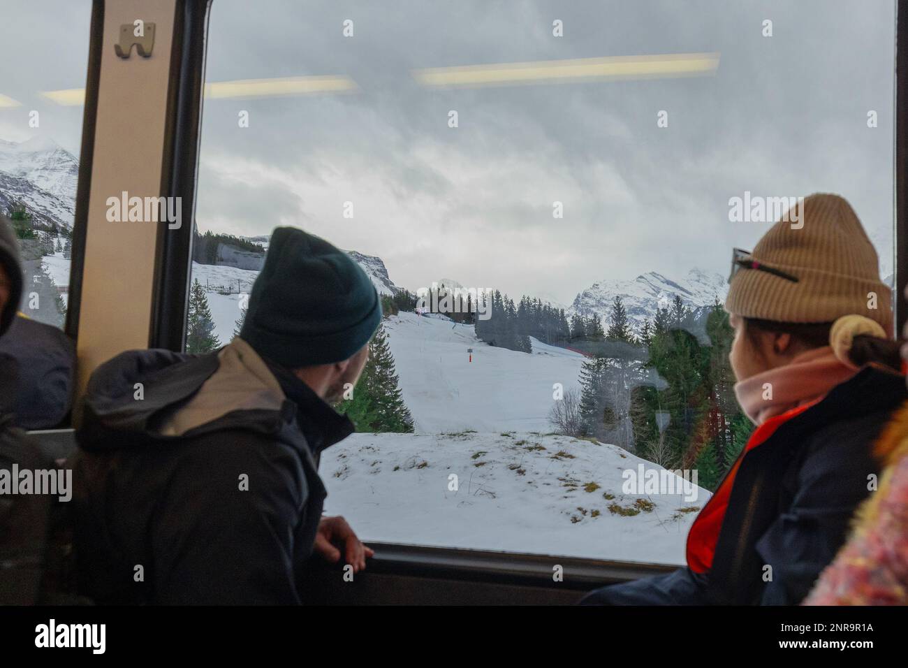 Unbekannte Menschen blicken aus dem Fenster eines Panoramaautos der Jungfrau-Schmalspurbahn an einem Wintertag. Stockfoto