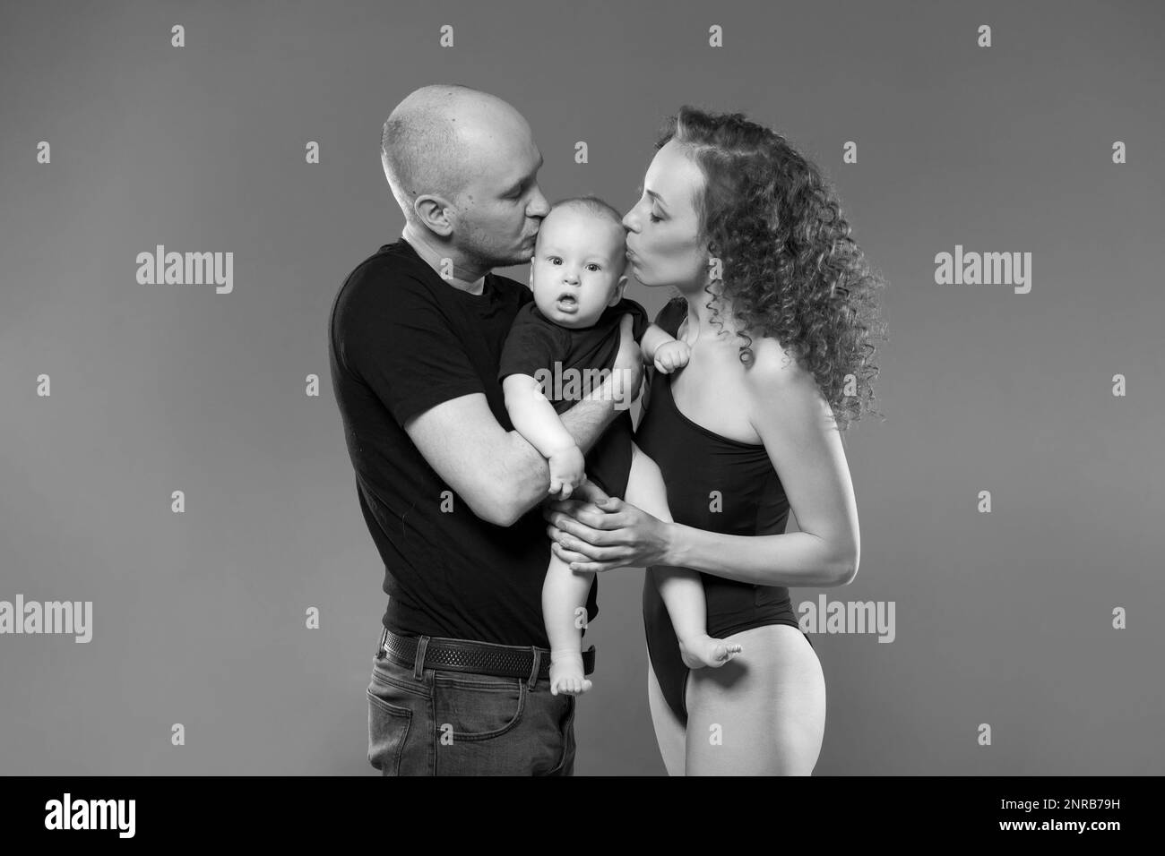 Junge Familie fotografiert mit Kleinkind. Vater hält das Kind in seinen Armen, Mutter steht zu. Familie bringt Liebe und Ehrfurcht einander zum Ausdruck. Familien- und Bildungskonzept. Im Studio Stockfoto