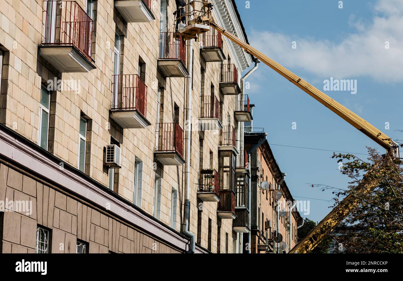 Männlicher Baumeister arbeitet in der Höhe in einer Hebevorrichtung. Bauarbeiter auf einem Kran in der Hubschaufel. Stockfoto