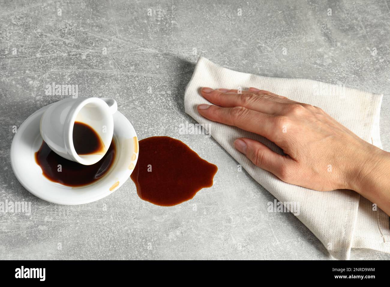 Eine Frau, die verschütteten Kaffee auf dem grauen Tisch abwischt Stockfoto