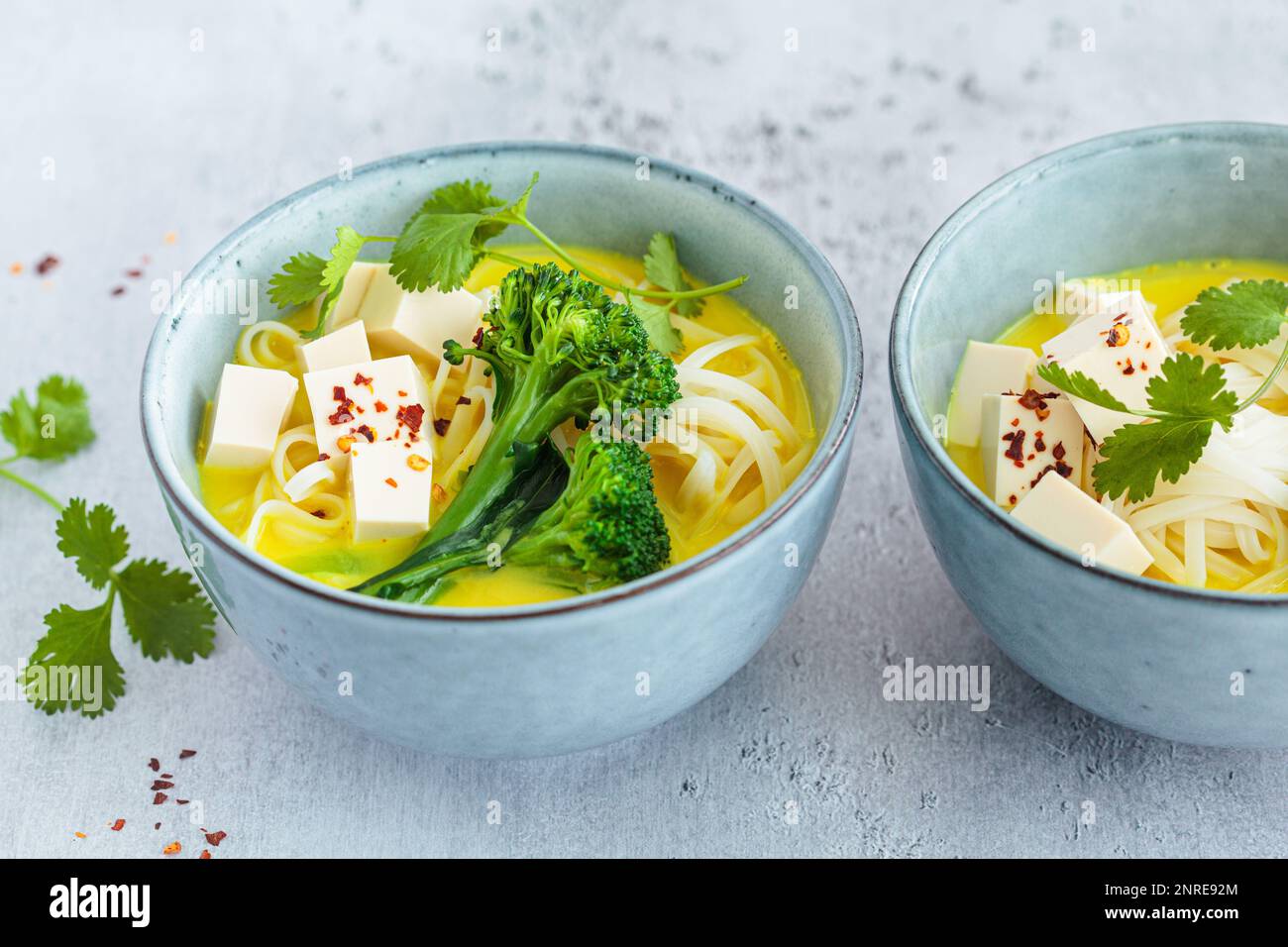 Vegane Currylaksa mit Reisnudeln, Brokkoli und Tofu in blauen Schüsseln, grauer Hintergrund. Stockfoto