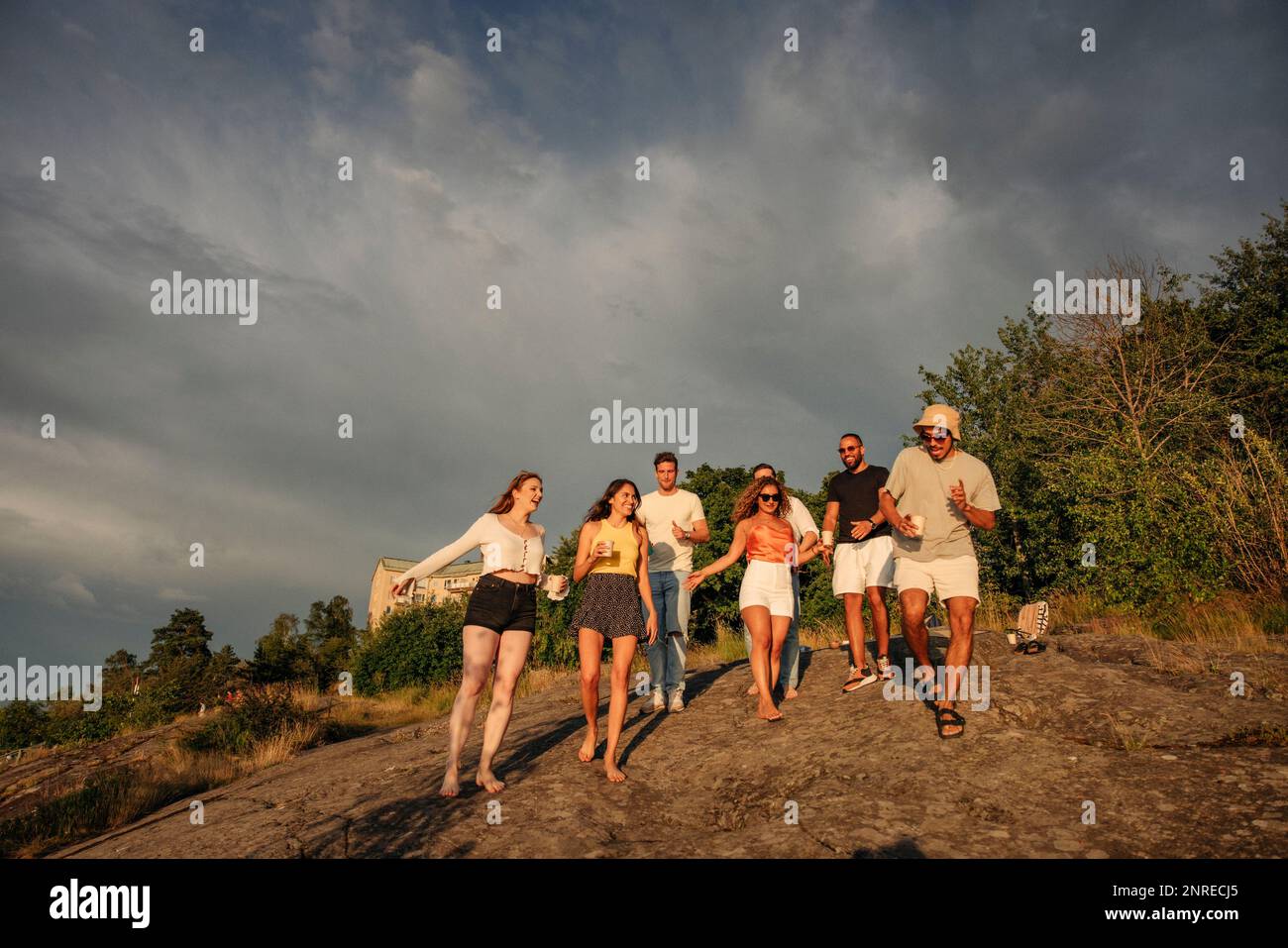 Männliche und weibliche Multirassenfreunde tanzen, während sie sich auf dem Felsen gegen den Himmel bewegen Stockfoto