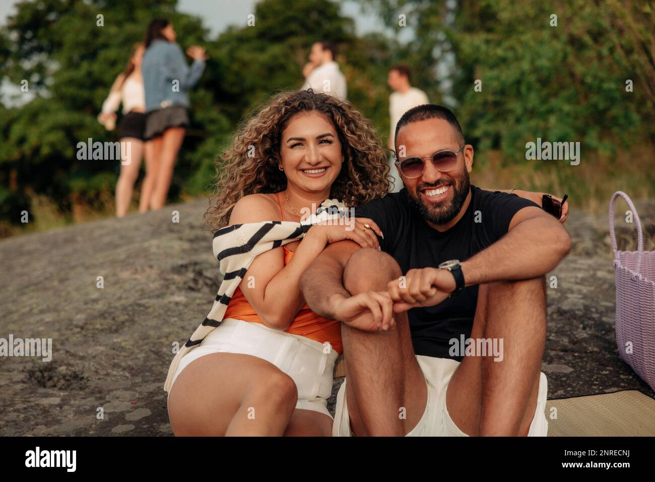 Porträt einer glücklichen Frau, die auf einem Stein sitzt, mit einem Mann, der beim Picknick eine Sonnenbrille trägt Stockfoto