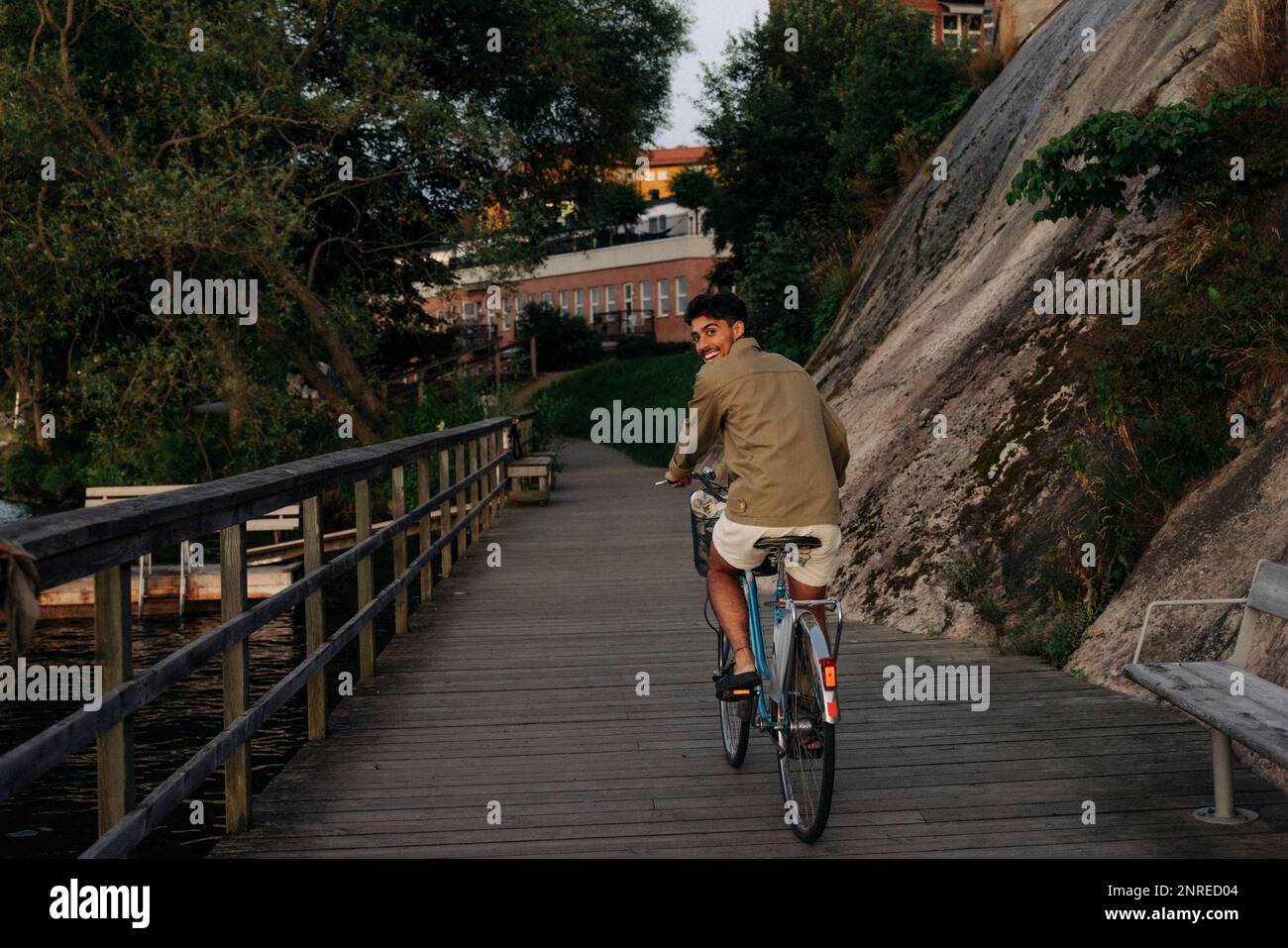 Glücklicher junger Mann, der über die Schulter blickte, während er auf dem Pier radelte Stockfoto