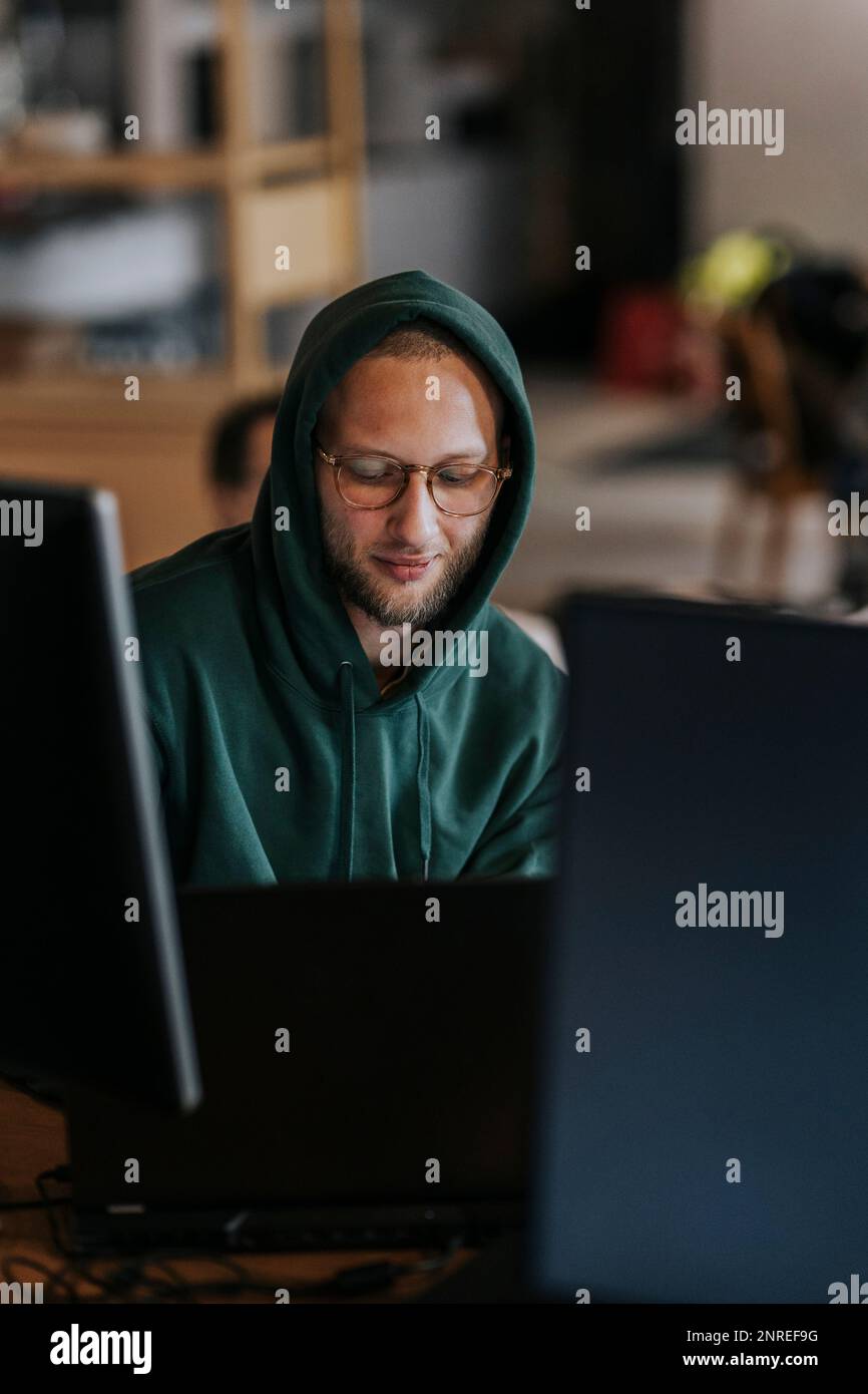 Junger männlicher Hacker, der in einer Startup-Firma an einem Laptop arbeitet Stockfoto
