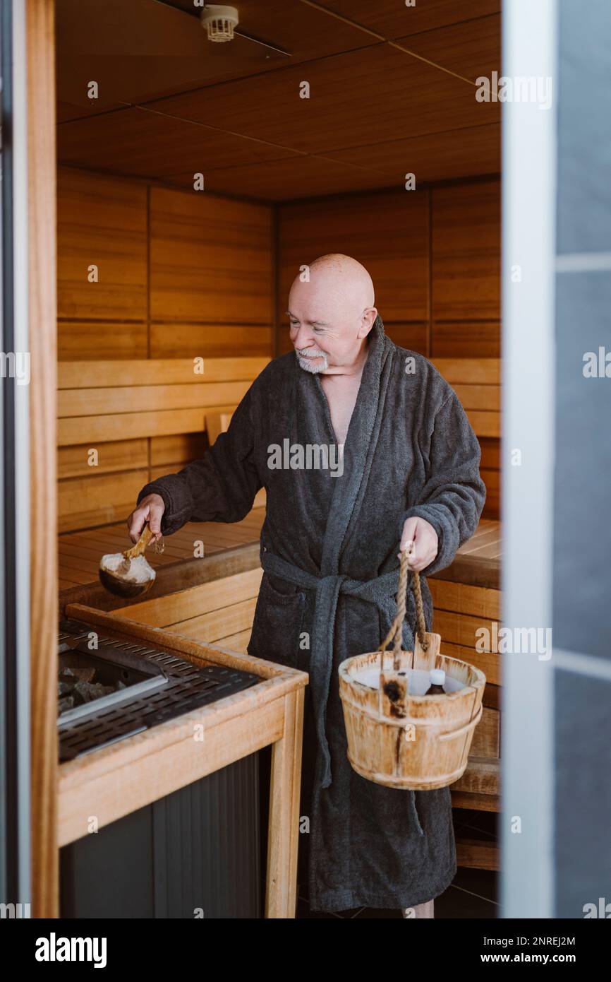 Ein älterer Mann, der in der Sauna heißes Stein in die Heizmaschine steckt Stockfoto