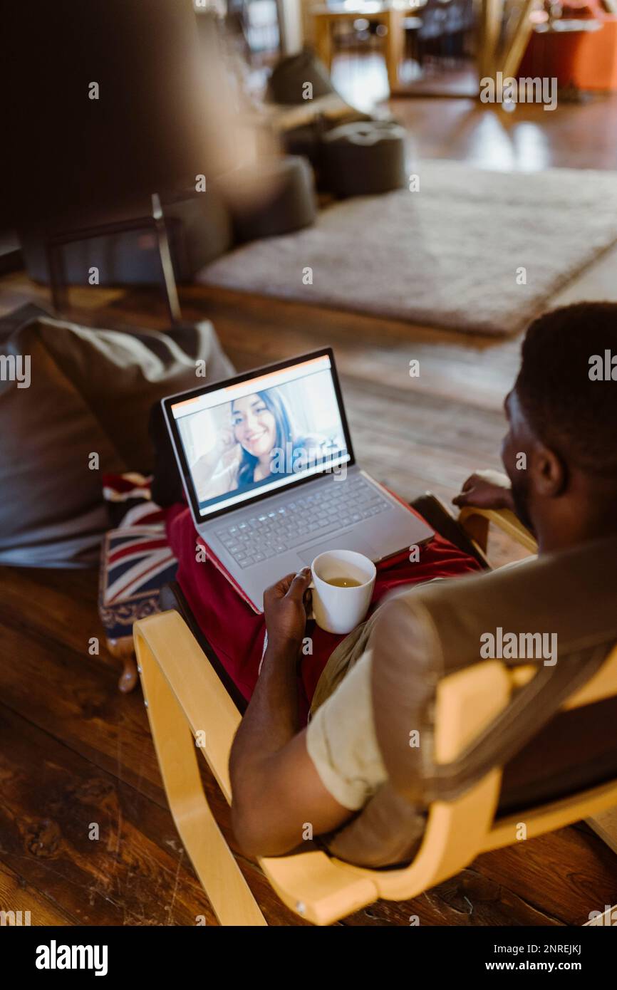 Ein Mann führt Videogespräche mit einer Frau über einen Laptop, während er zu Hause auf einem Stuhl sitzt Stockfoto
