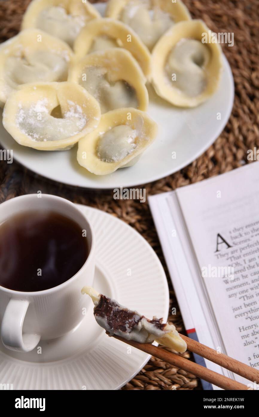 Fotos von vielen Schokoladensüßen in Form von weißen und dunklen Schokoladenknödeln liegen auf einem Teller neben einem Buch und einer Kaffeetasse, es gibt Dampf über t Stockfoto