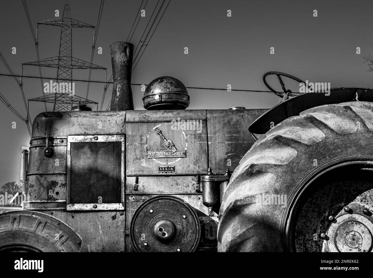 Ein klassischer Feldmarshall-Traktor, der bei einer Rallye in Wisborough Green, Großbritannien, unter einem Strompylon und einer Übertragungslinie geparkt wurde. Stockfoto