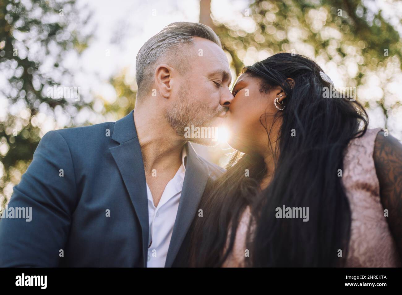 Ein erwachsener Bräutigam mit Hintergrundbeleuchtung küsst die junge Braut während der Hochzeit Stockfoto