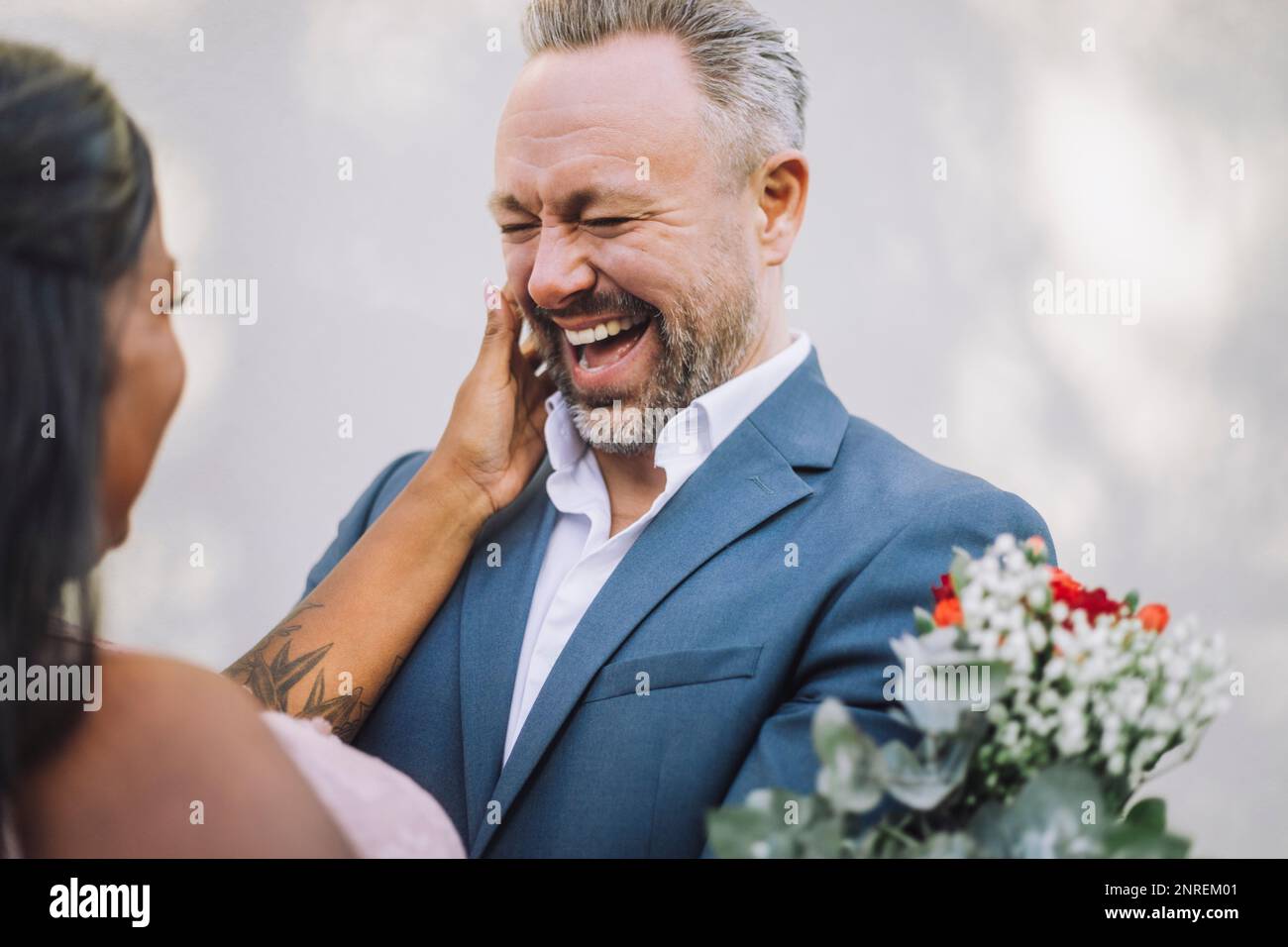 Reifer Bräutigam, der lacht, während er die Braut an der Wand ansieht Stockfoto