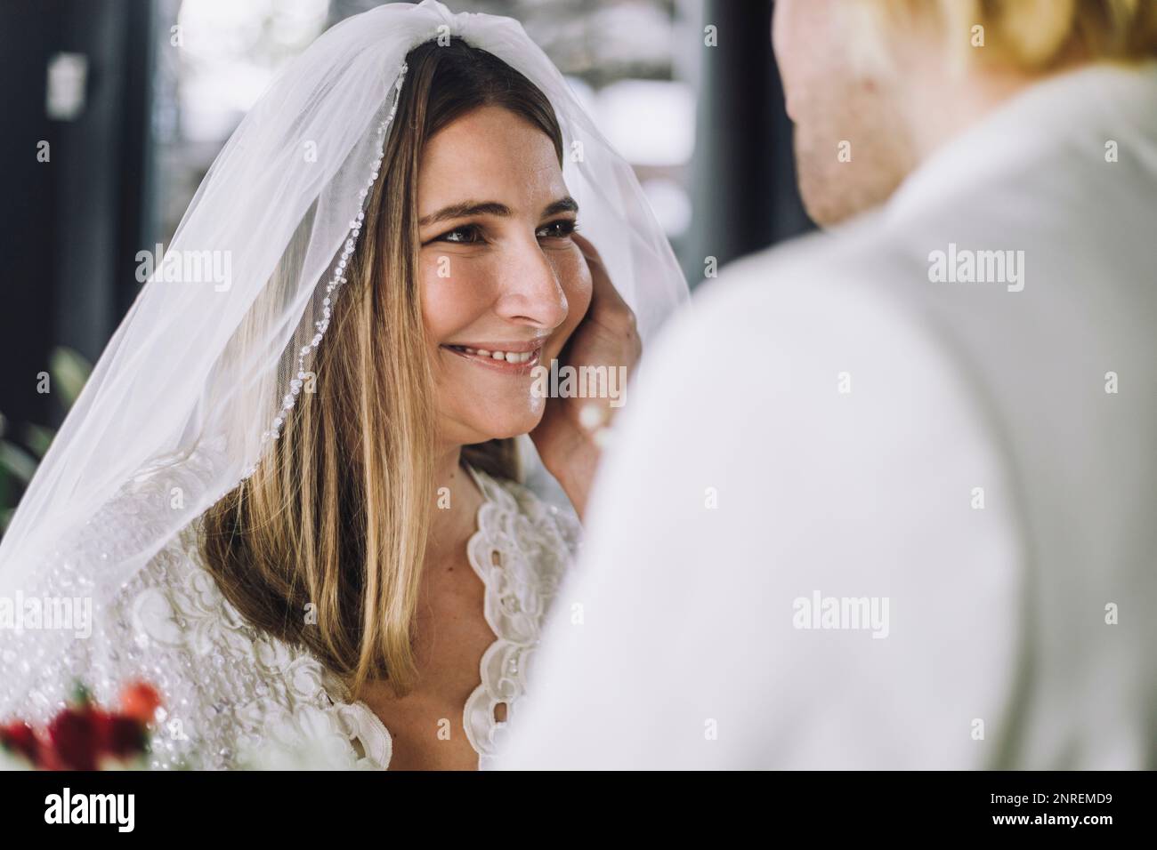 Glückliche, mittelgroße Braut im Hochzeitskleid, die den Bräutigam anschaut Stockfoto