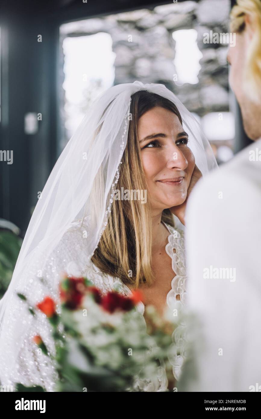 Lächelnde mittelgroße Braut im Hochzeitskleid, die den Bräutigam ansieht Stockfoto