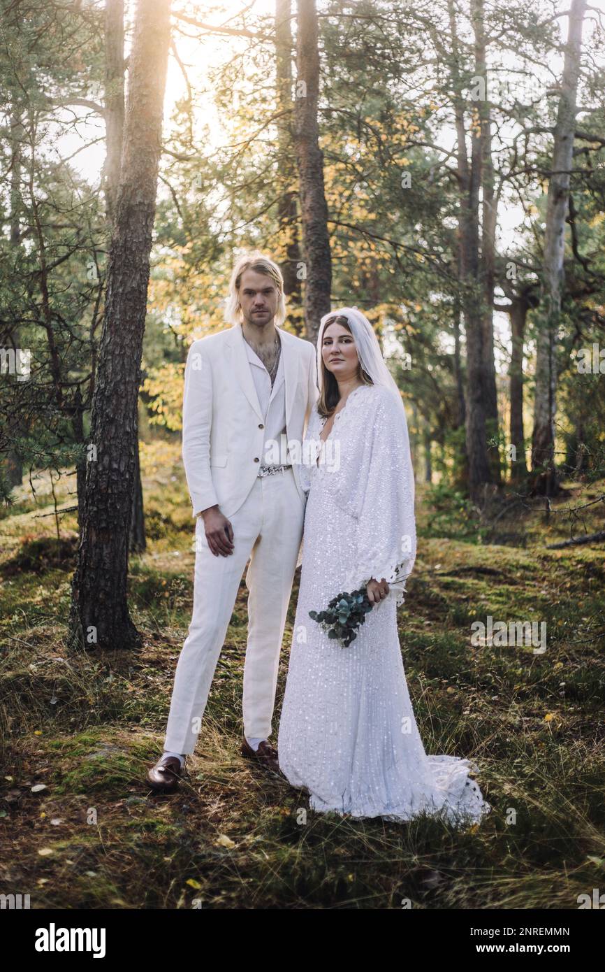 Porträt von gut gekleideter Braut und Bräutigam, die bei der Hochzeit an Bäumen im Wald standen Stockfoto