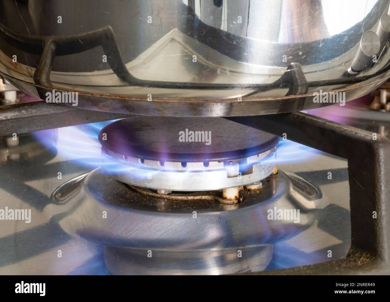 Blaue Gasstrahlen, die unter einem Stahltopf auf einem Kochfeld brennen Stockfoto