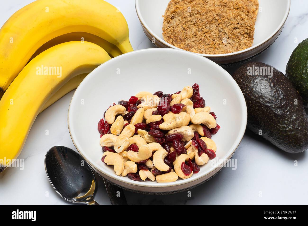 Schale mit Cashews und Cranberrys neben Bananen-Avocados und eine Schüssel mit zwei Frühstückskeksen Stockfoto