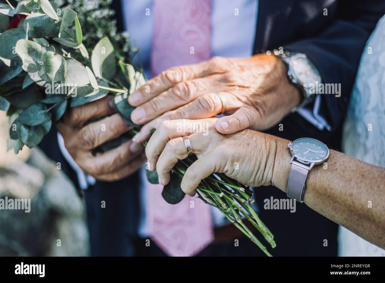Zugeschnittenes Bild eines frisch verheirateten Paares, das Ringe zeigt, während er während der Hochzeitszeremonie einen Strauß hält Stockfoto
