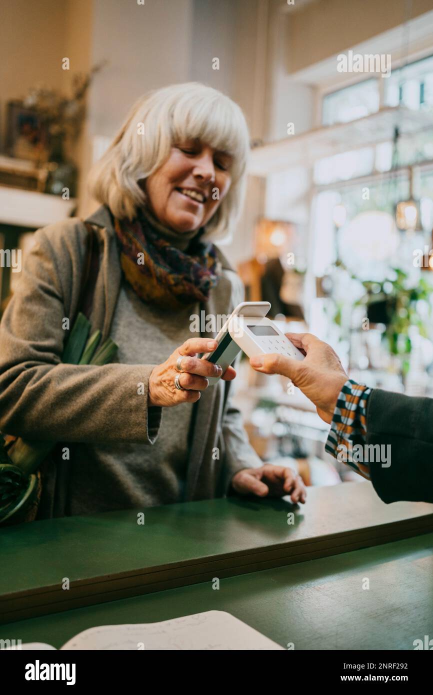 Seniorin bezahlt per Tap-to-Pay-Methode, während sie im Geschäft einkauft Stockfoto