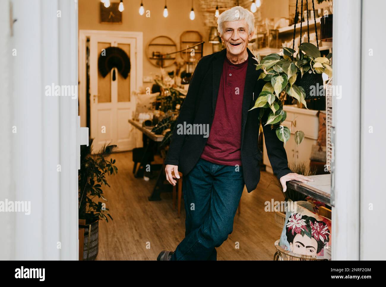 Porträt eines glücklichen Senior-Besitzers, der sich im Laden auf den Tisch lehnt Stockfoto