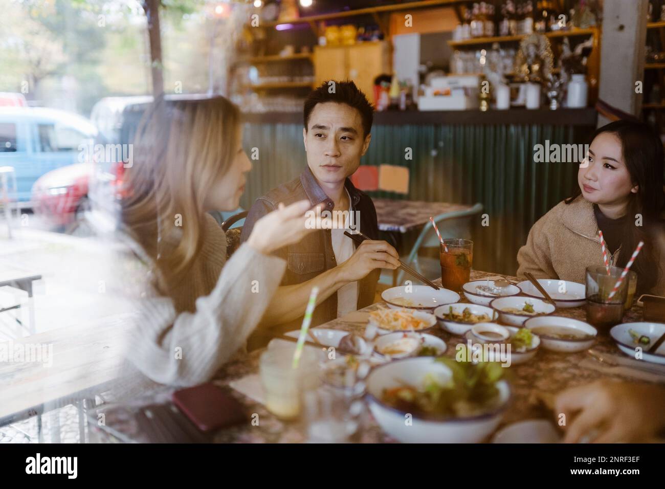 Männliche und weibliche Freunde, die sich unterhalten, während sie im Restaurant sitzen und durch ein Glasfenster gesehen werden Stockfoto