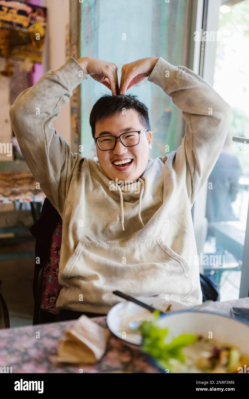 Ein glücklicher junger Mann, der sich im Restaurant mit den Händen ein Herz geformt hat Stockfoto