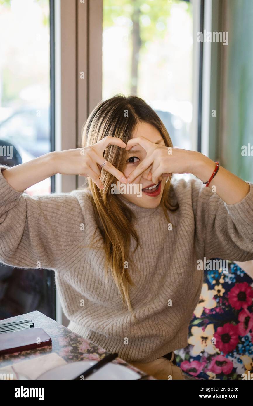 Porträt einer Frau, die durch eine herzförmige Geste im Restaurant schaut Stockfoto