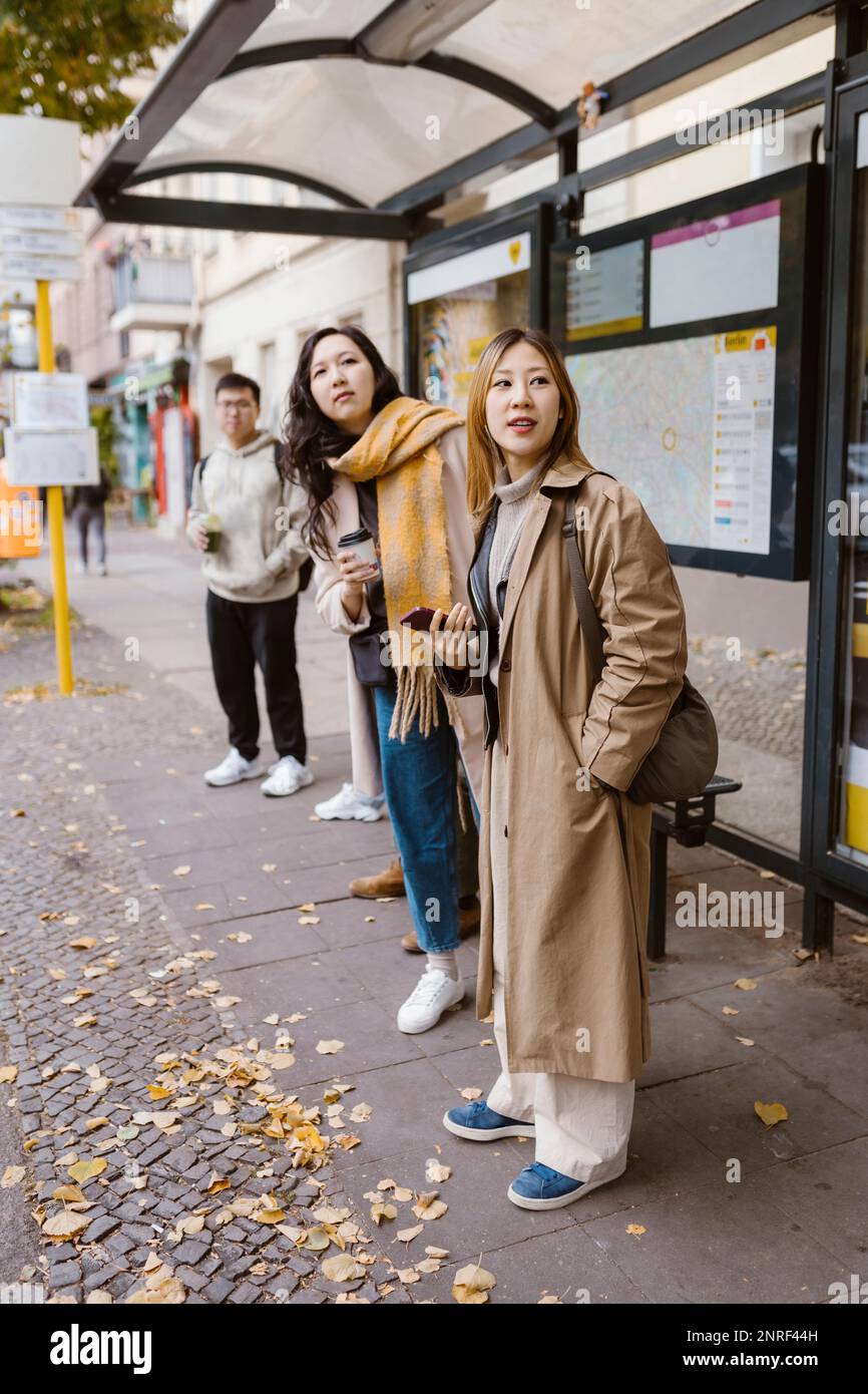 Weibliche Freunde, die wegschauen, während sie an der Bushaltestelle warten Stockfoto