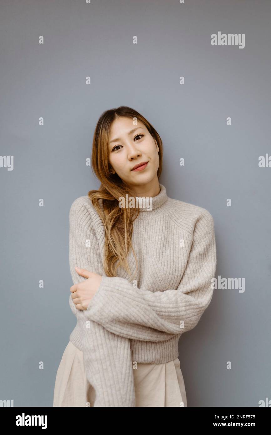Porträt einer jungen Frau, die einen Pullover trägt und vor grauem Hintergrund steht Stockfoto