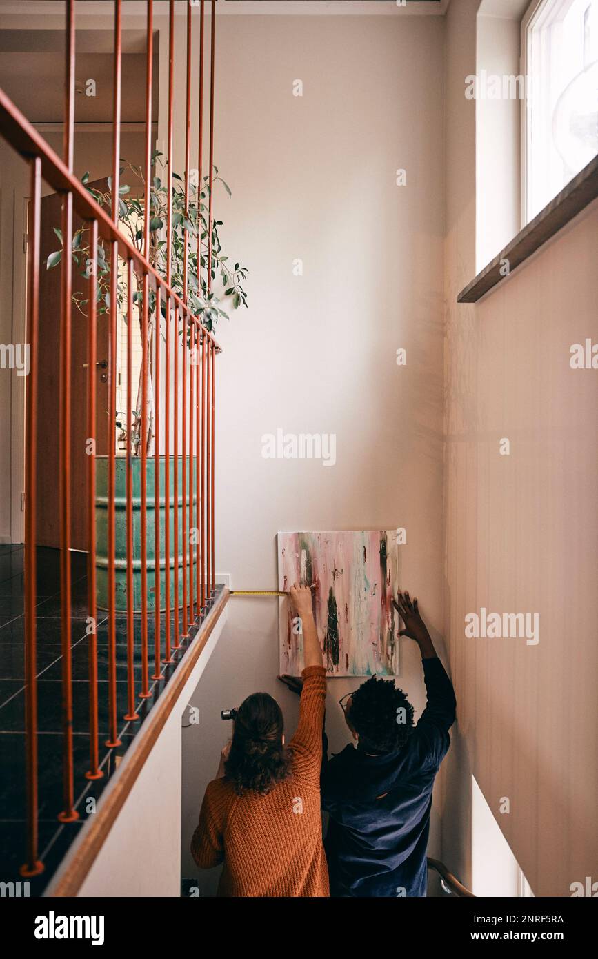 Rückansicht des Paares, das Messungen durchführt, während es zu Hause an der Wand lackiert Stockfoto