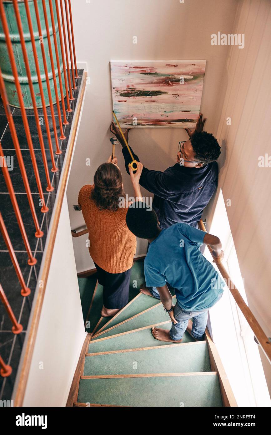 Aus einem großen Blickwinkel kann die Familie sich gegenseitig helfen, während sie zu Hause Malerei an der Wand aufhängt Stockfoto