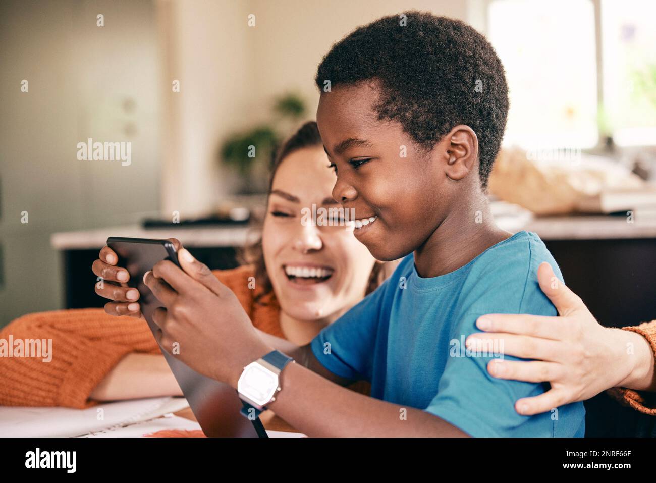Glückliche Mutter mit Arm um den Sohn, die sich zu Hause ein digitales Tablet ansieht Stockfoto