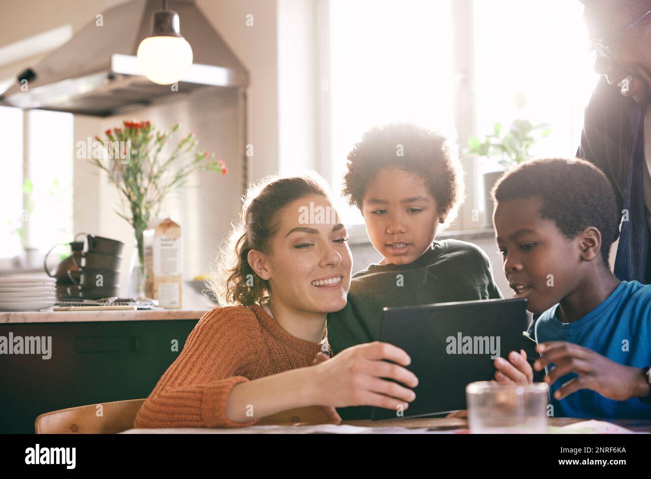 Lächelnde Mutter, die sich ein digitales Tablet ansieht, mit Söhnen zu Hause Stockfoto