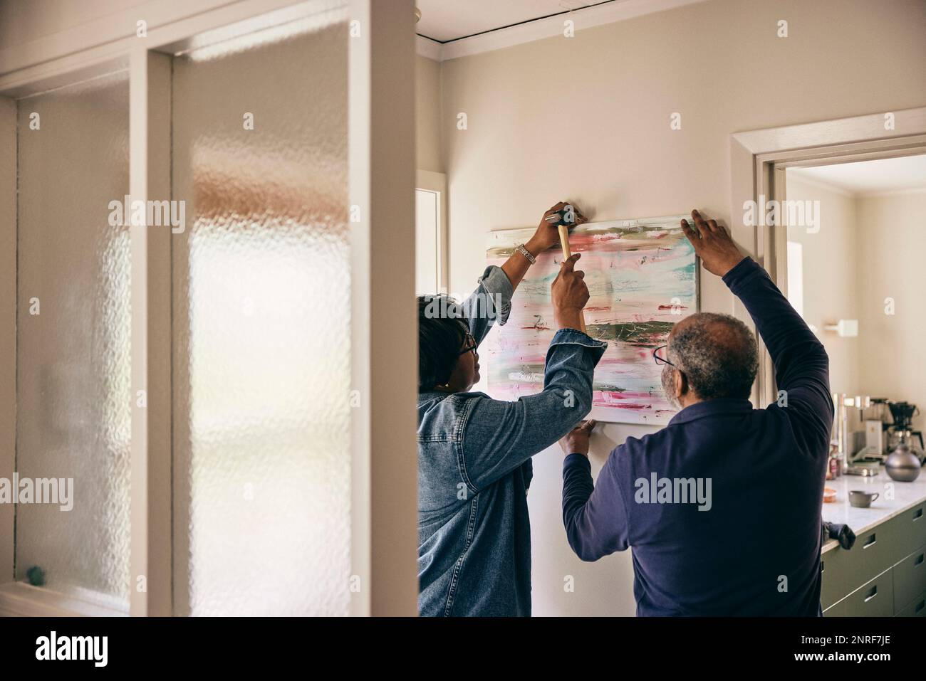 Rückansicht eines Seniorenmannes, der einer Frau hilft, zu Hause ein Bild an der Wand aufzuhängen Stockfoto