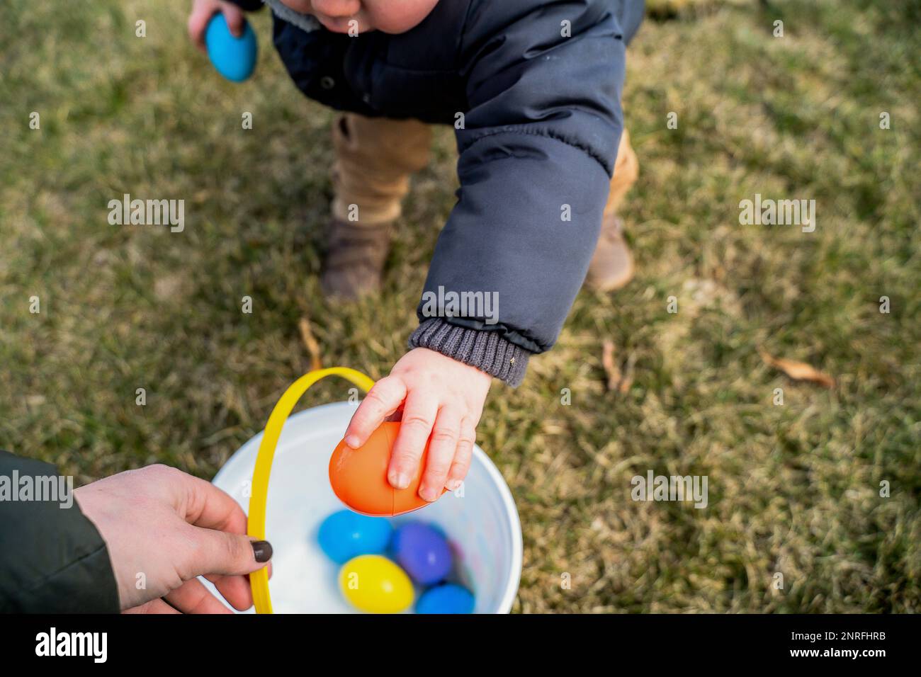 Baby Boy legt buntes osterei in Plastikeimer Stockfoto