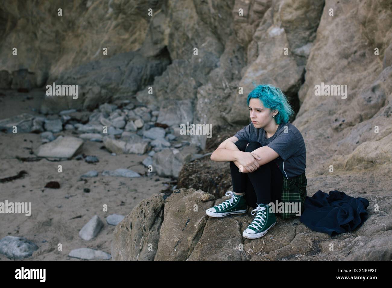 Moody Teenager mit blauen Haaren sitzt auf einem Felsen am Strand Stockfoto