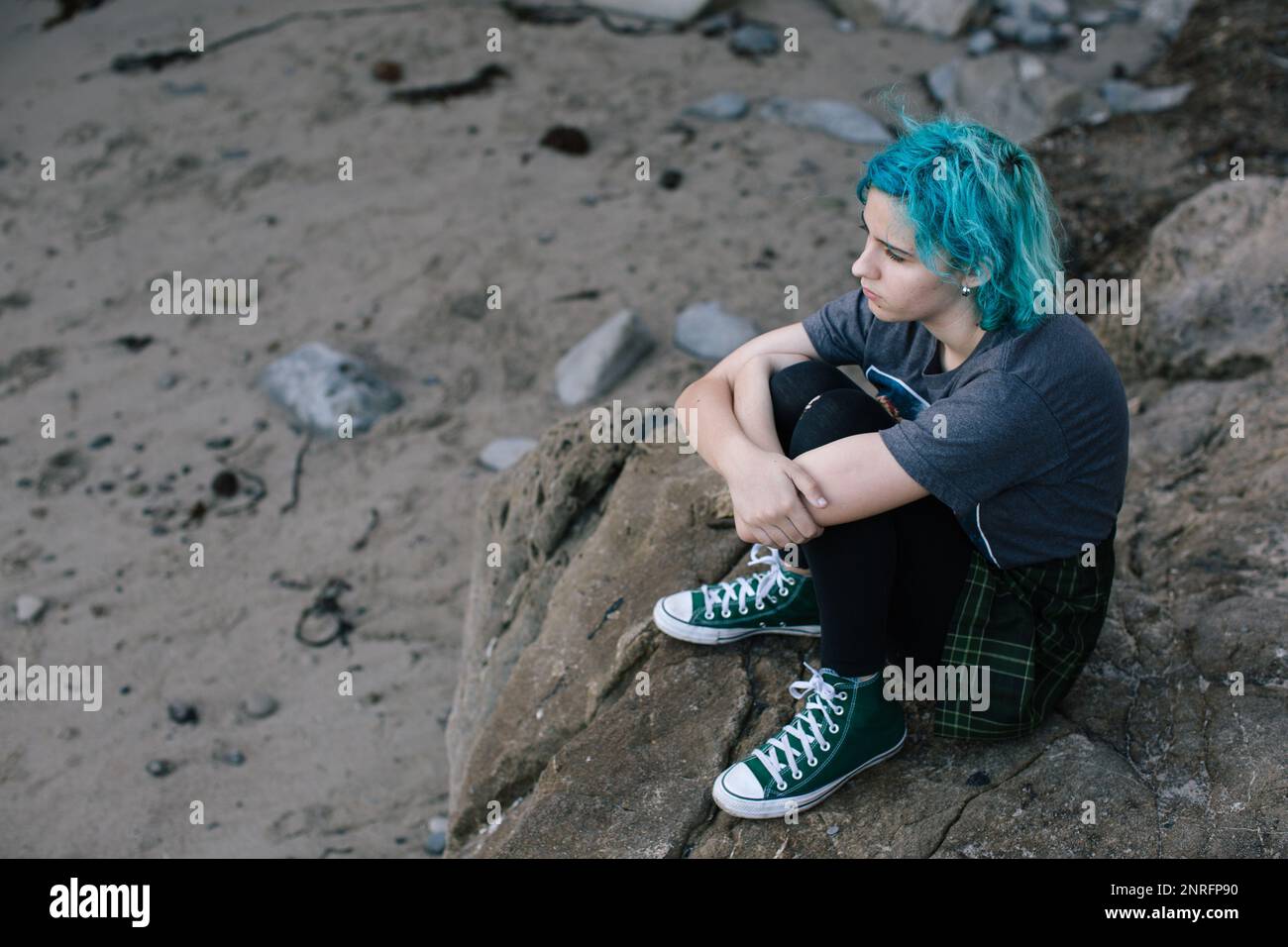 Ein Mädchen mit blauen Haaren sitzt auf einem Felsen am Strand Stockfoto