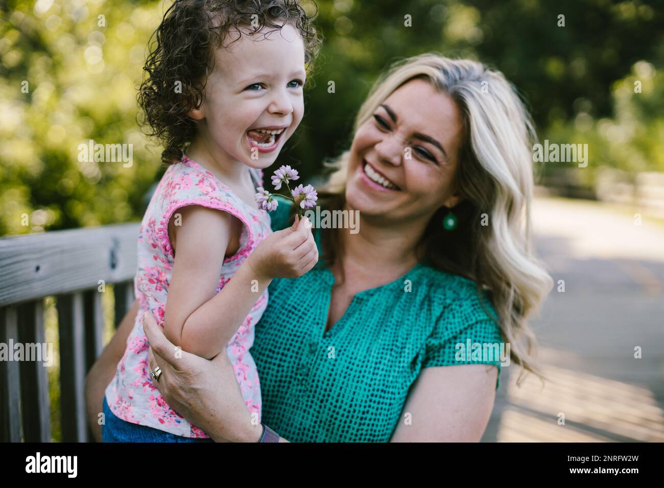 Mama hält und lacht mit der Tochter, die Blumen gepflückt hat Stockfoto