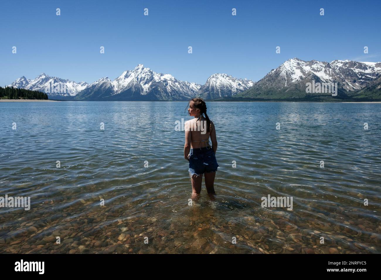 Ein Mädchen betritt den See in der Nähe der schneebedeckten Berge Stockfoto