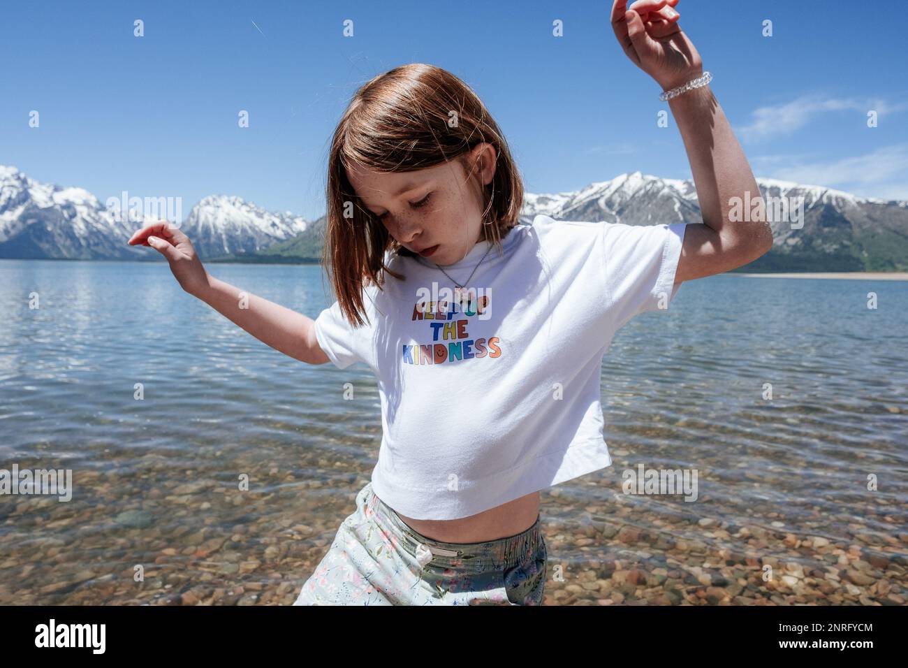 Ein junges Mädchen tanzt am Seeufer in der Nähe verschneiter Berge Stockfoto