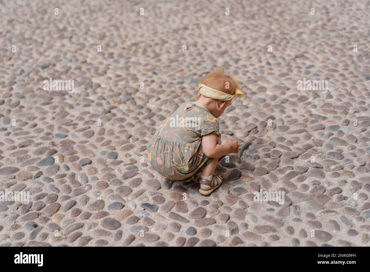 Das weiße Mädchen spielt auf den Pflastersteinen auf dem alten Platz Stockfoto