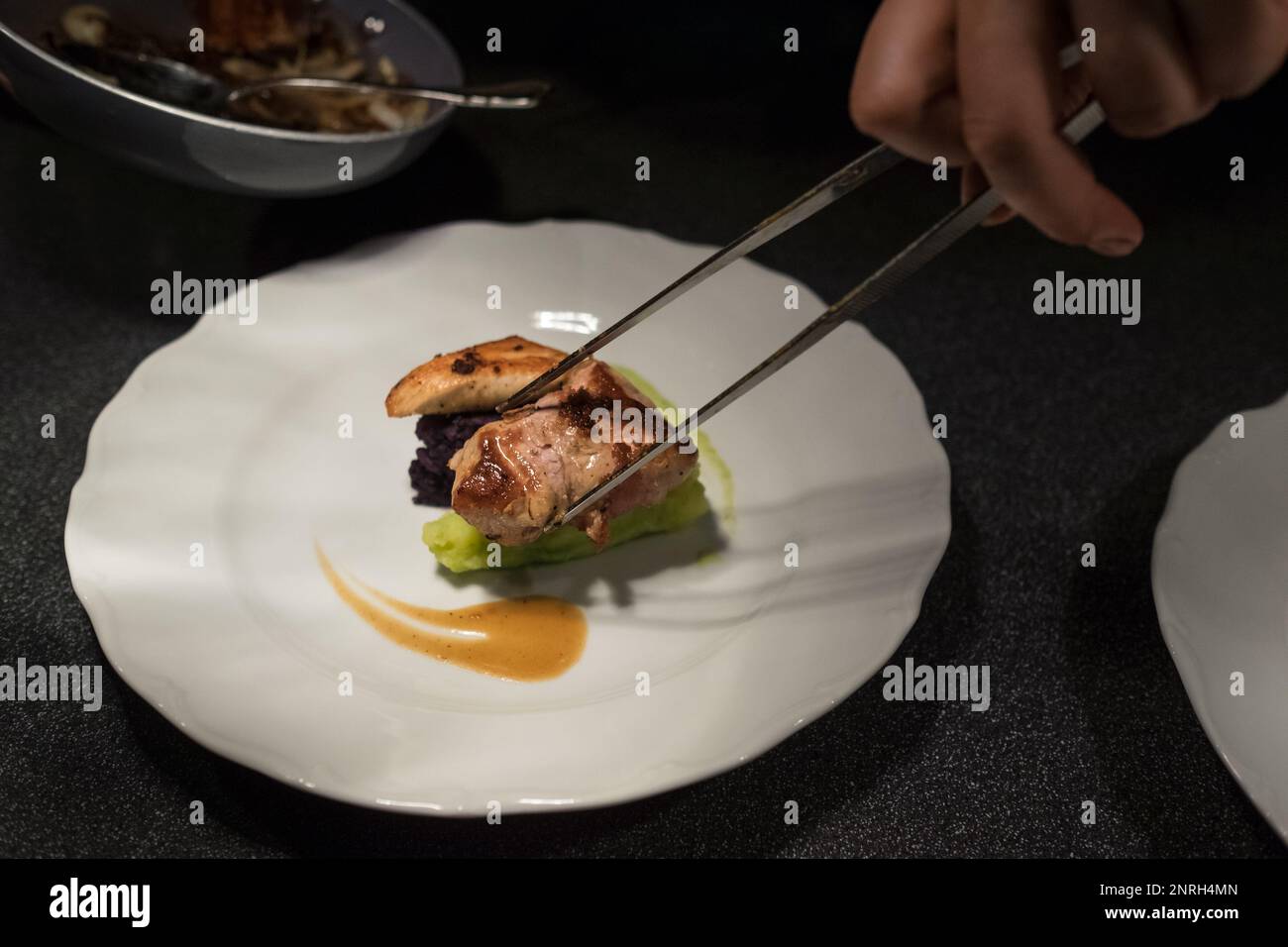 Chef Koch setzen gegrilltes Fleischstück mit einer Pinzette auf grünes Gemüse püriert weißen Teller mit Sauce. Gesunde Mahlzeiten Zubereitung, Kochen oder Kleinbus Stockfoto