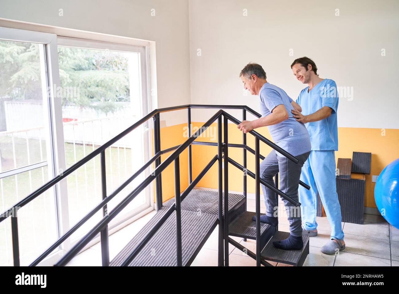 Lächelnder männlicher Physiotherapeut, der älteren Mann bei der Kletterrampe im Rehabilitationszentrum unterstützt Stockfoto