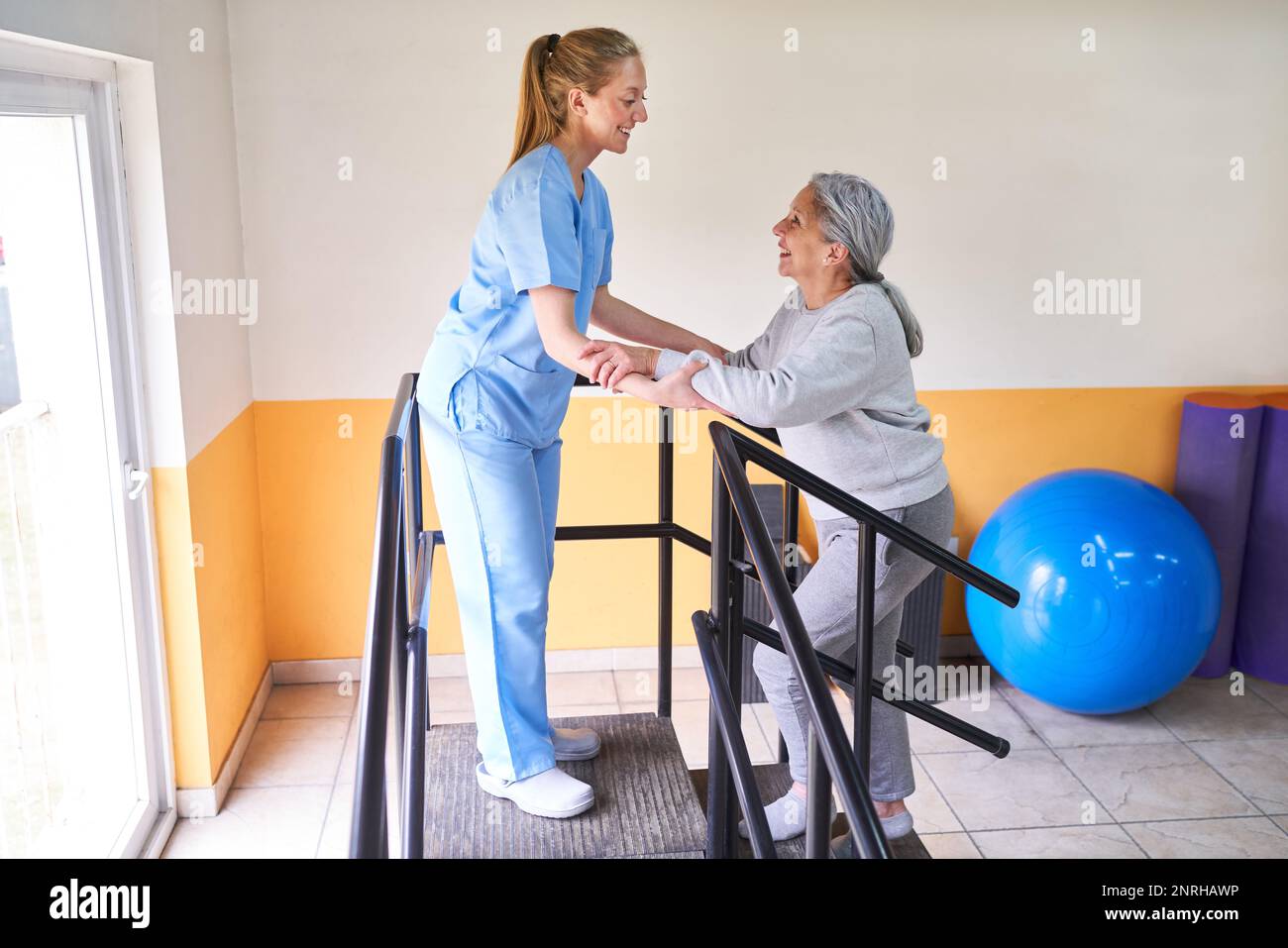 Lächelnde junge Physiotherapeutin, die ältere Frau in der Kletterrampe des Rehabilitationszentrums unterstützt Stockfoto