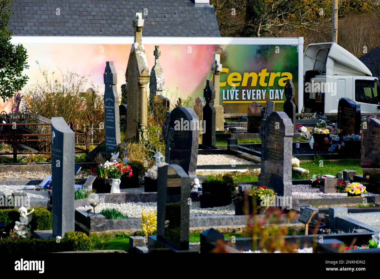 Ardara, County Donegal, Irland. 27. Februar 2023 Ein Lieferwagen aus dem Supermarkt mit Centra-Werbung schafft eine ironische Nebeneinanderstellung mit einem Friedhof in der Stadt. Kredit: Richard Wayman/Alamy Live News Stockfoto